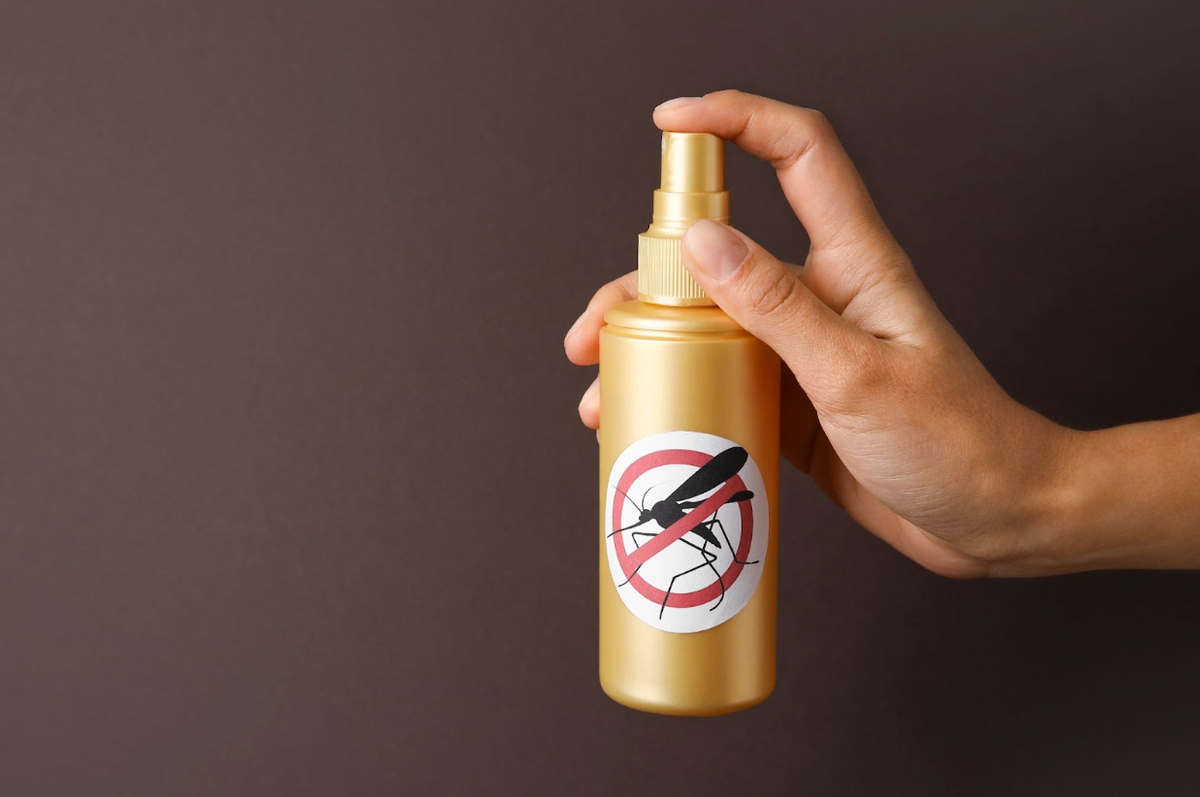 Woman with mosquito repellent spray on dark background